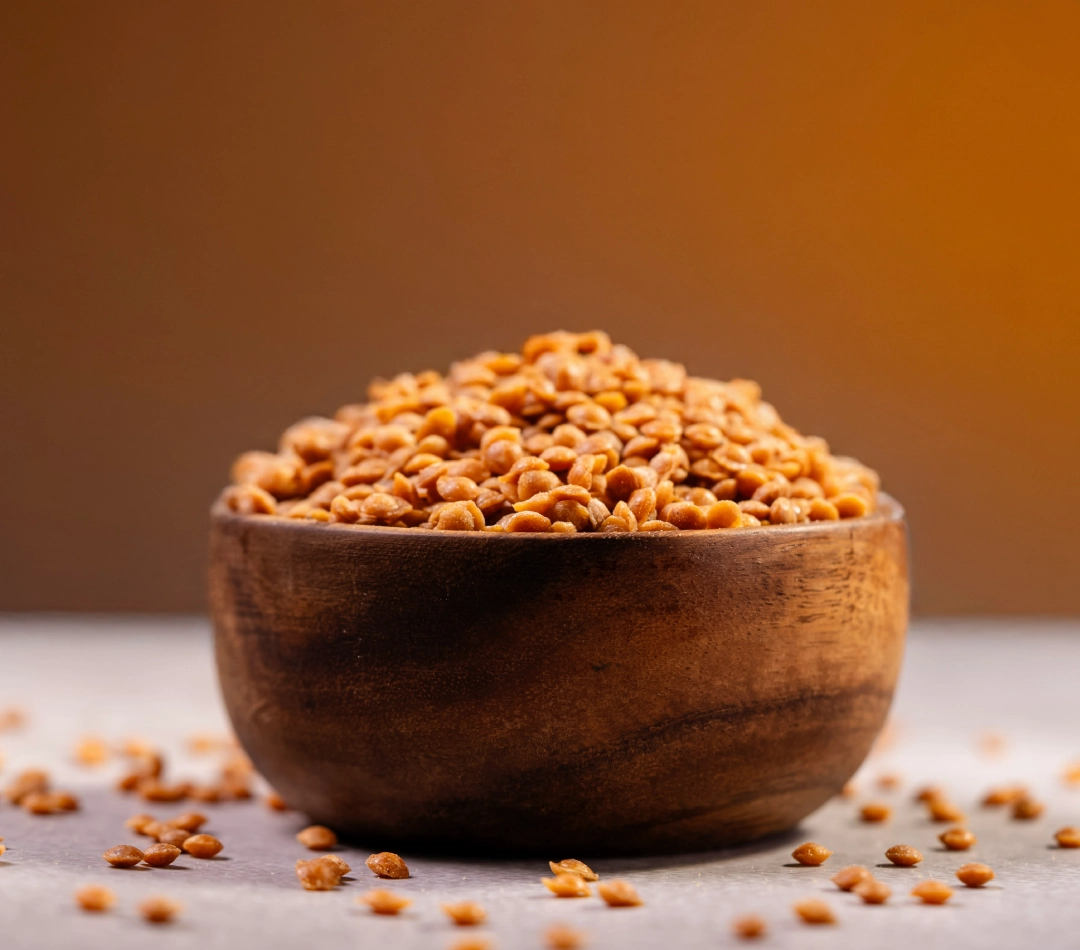 A wooden bowl filled with 4mm butterscotch nuts or flakes, displayed against a warm background on a textured surface.