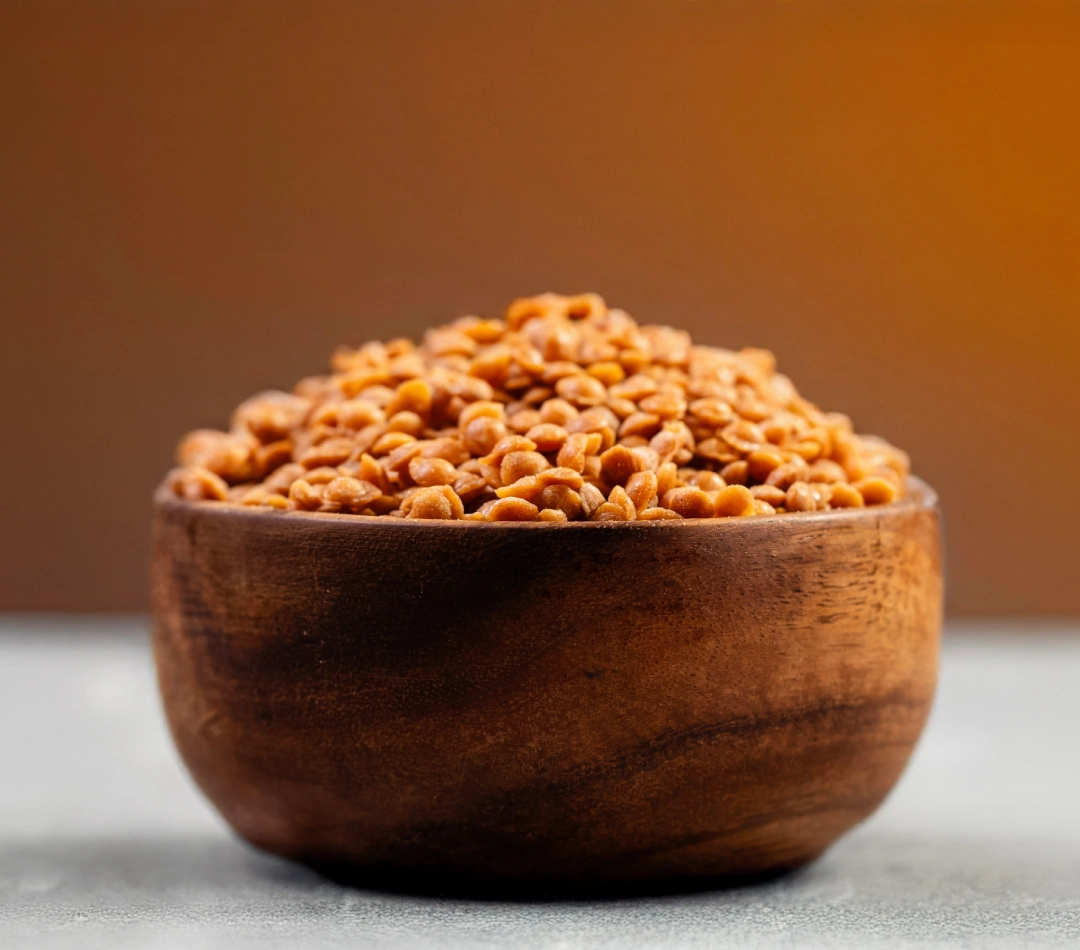 A wooden bowl filled with 4mm butterscotch nuts or flakes, displayed against a warm background on a textured surface.